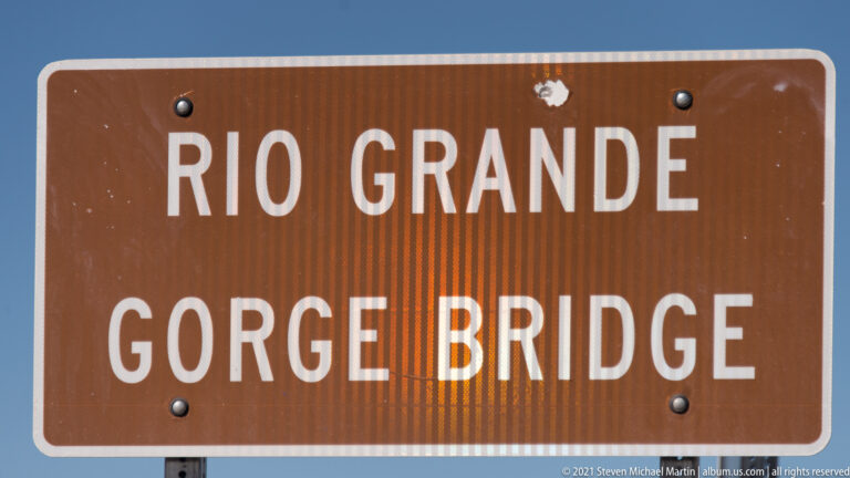 A brown highway sign with white letters reads “Rio Grande Gorge Bridge.”