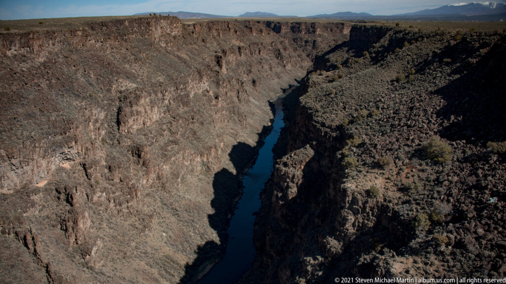 A dark blue river runs through a narrow gorge with steep, scrub-covered walls.
