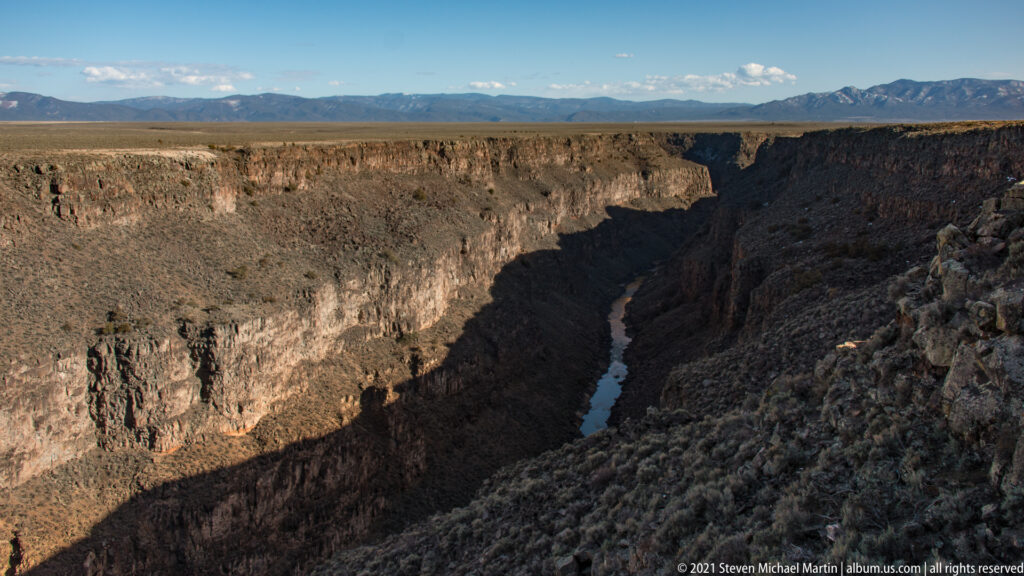 A narrow river winds through a steep gorge, with sunlight on the upper cliffs and shadow below.