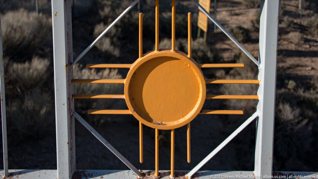 A golden Zia symbol is mounted in a white geometric frame on the bridge railing.