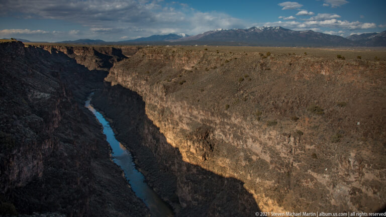 A blue-green river winds through a deep gorge beneath an open plateau and distant mountains.