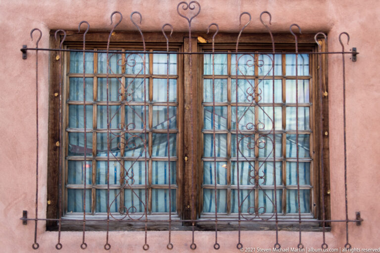 A decorative iron grille with loops and heart-shaped curls covers two wood-framed windows.