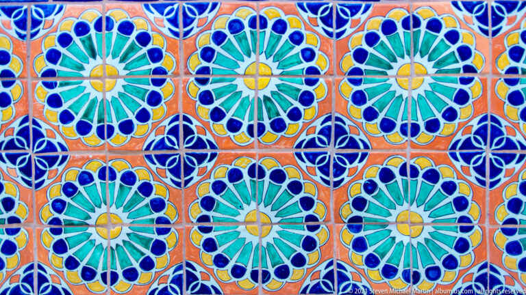 Square tiles repeat blue and green rosettes linked by dark blue lines on an orange ground.