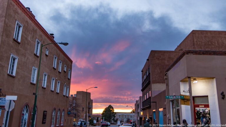 Pink sunset clouds glow above a street framed by stucco buildings and a Galisteo street sign.