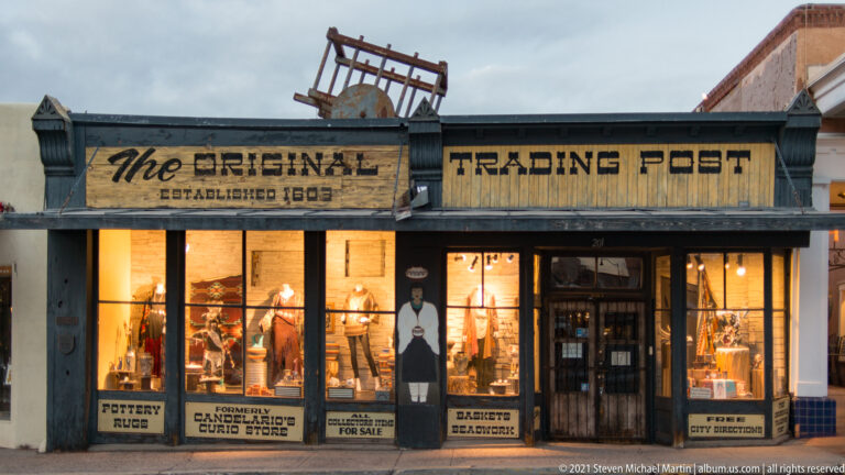 A timber storefront reads “The Original Trading Post” and displays pottery, rugs, and jewelry signs.