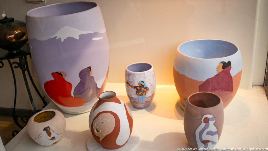 Painted ceramic vessels of varying shapes display simplified human figures in bold colors.