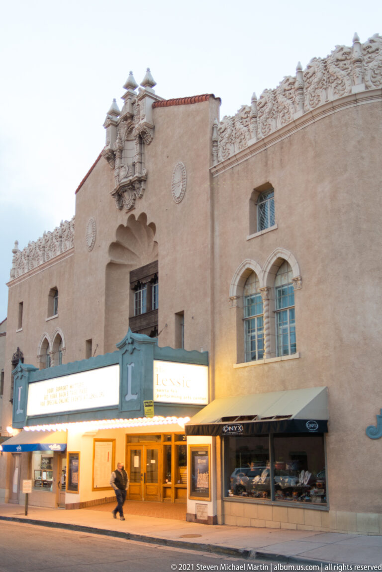 An ornate stucco facade with arched windows and sculpted parapet rises above a lit marquee.