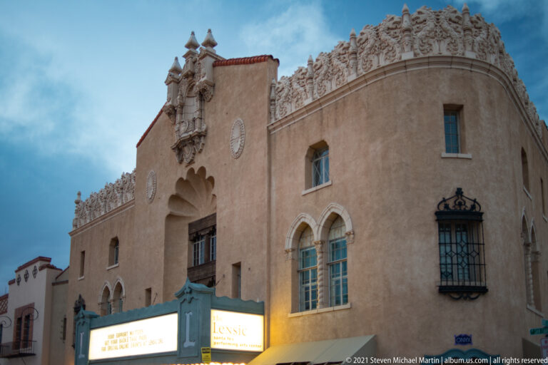 An angled view shows arched windows, sculpted parapet details, and a glowing marquee below.