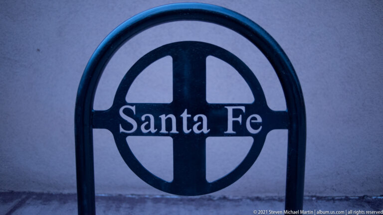 A circular black sign on a pale wall displays “Santa Fe” in white lettering.