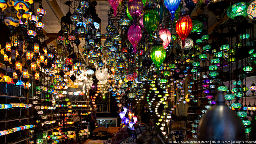 Colorful glass lanterns hang densely from the ceiling inside a dimly lit shop.