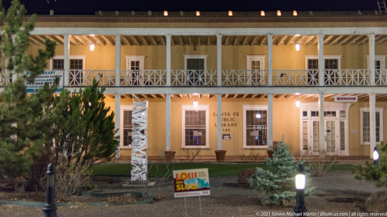 Santa Fe Public Library at night, with two wooden galleries, cross-braced railings, and lit windows.