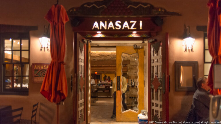 Illuminated “ANASAZI” sign hangs above a curtained entrance with warm wall lights.