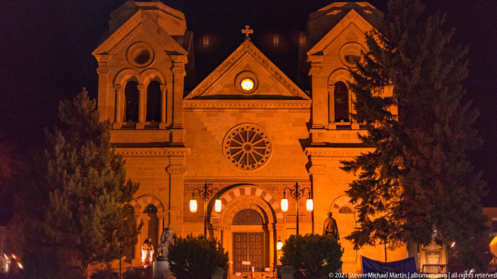 Twin-towered Cathedral Basilica façade glows at night, with its rose window and entrance centered.
