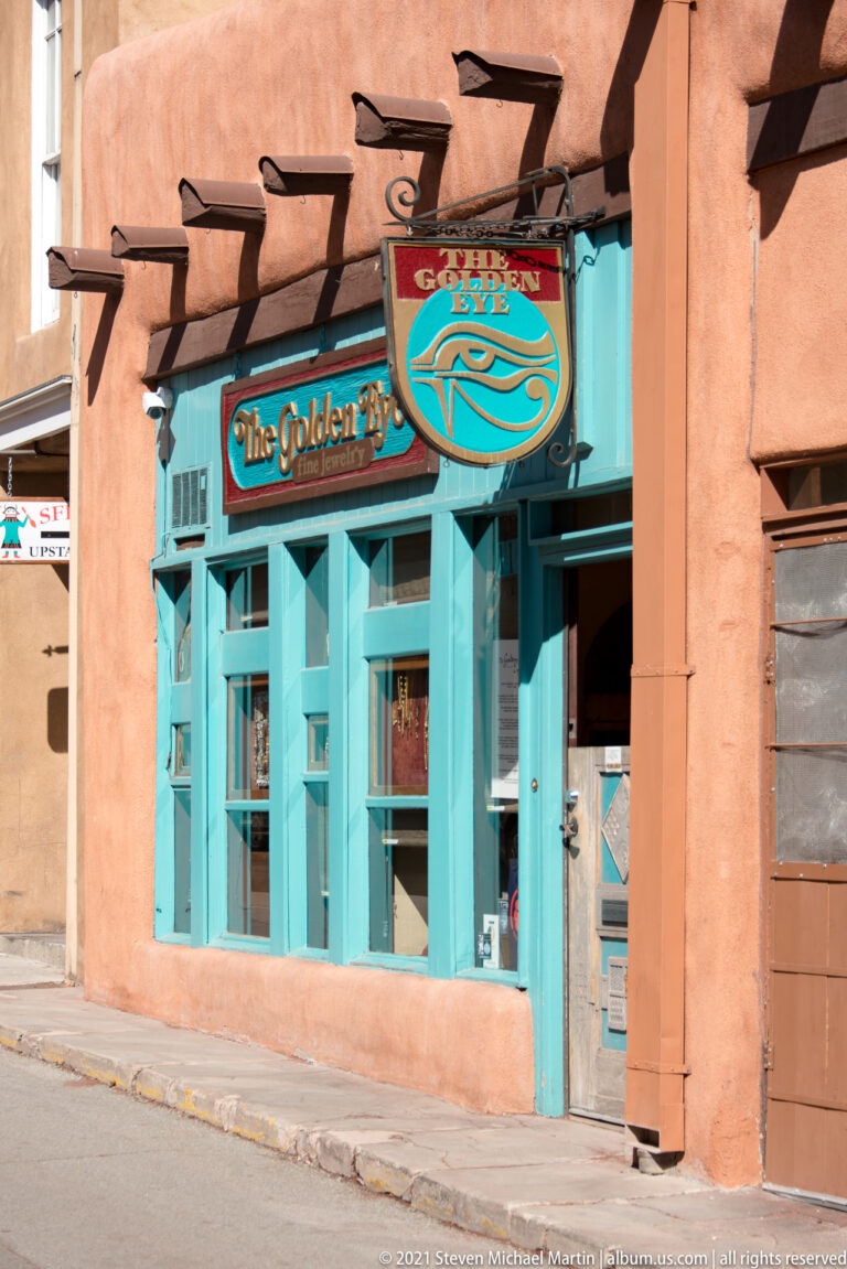 A turquoise storefront and hanging sign stand out against a salmon stucco building.