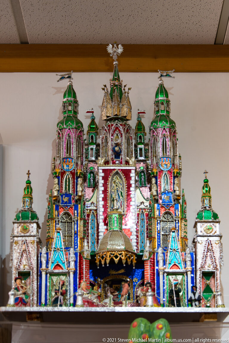 A colorful miniature church-like structure has twin towers, arches, painted figures, and a central doorway.