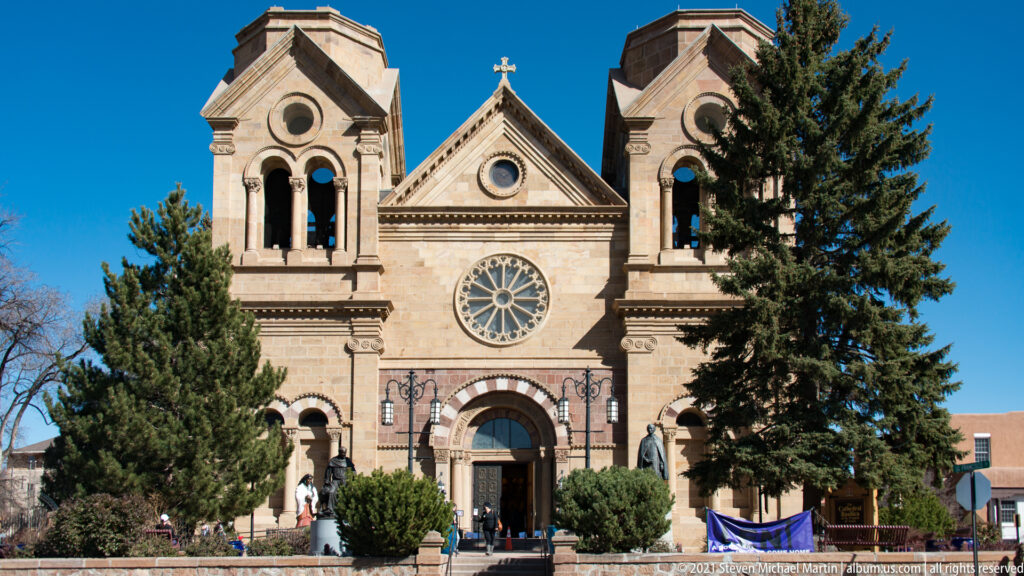 A stone cathedral facade has twin towers, a rose window, an arched entrance, and a central cross.