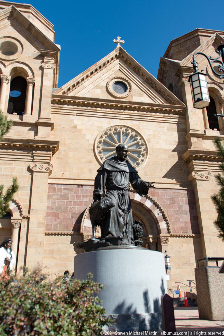 A bronze robed figure with an outstretched arm stands before a cathedral doorway and rose window.