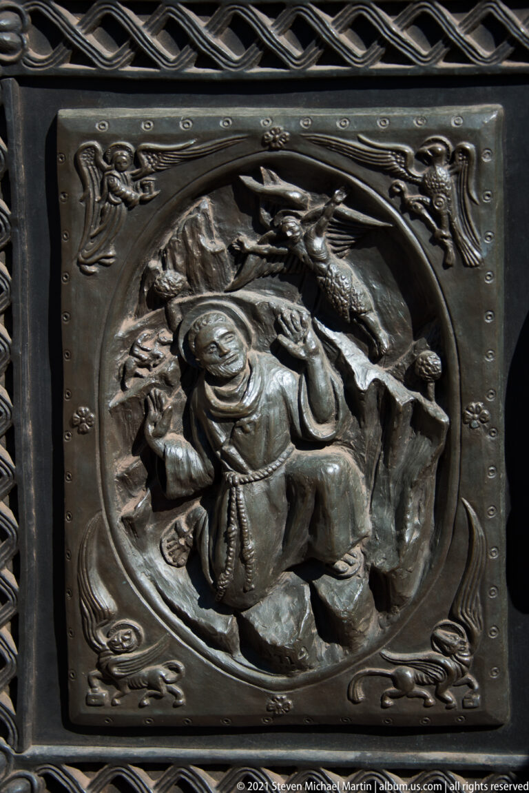 A bronze door relief shows a central robed figure surrounded by smaller figures and animals.