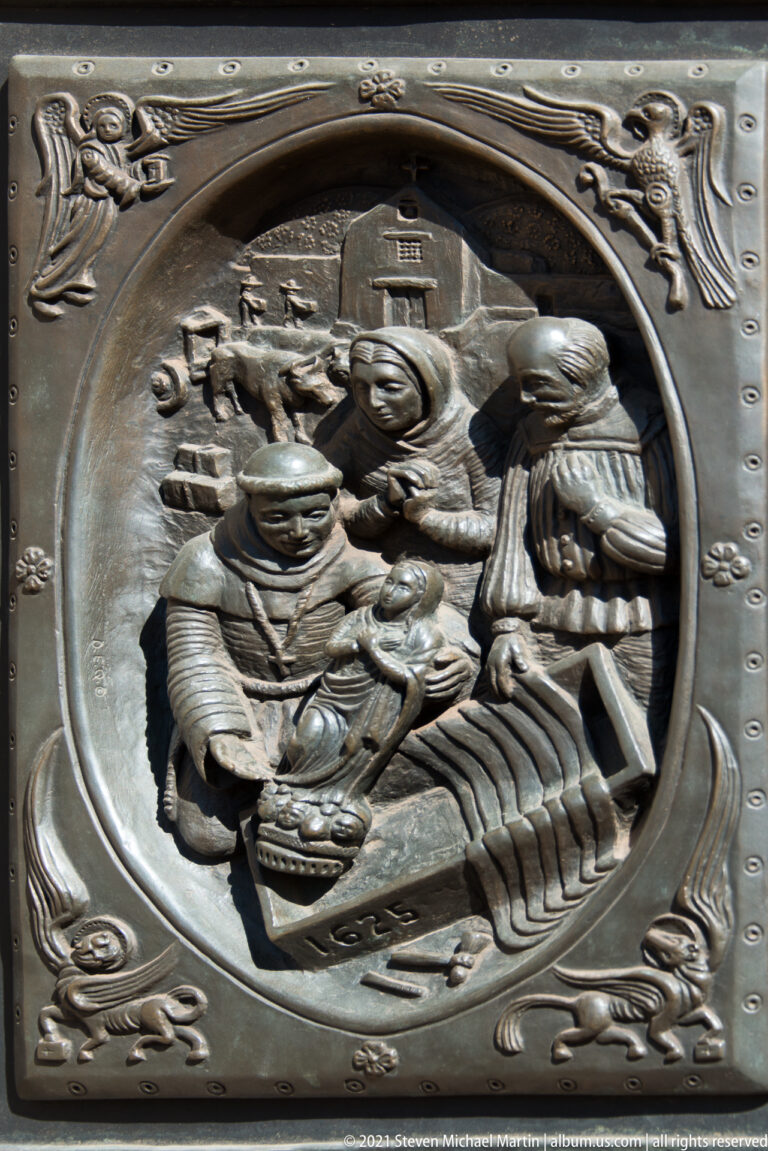 A bronze door panel shows several figures gathered around a seated person in an oval frame.
