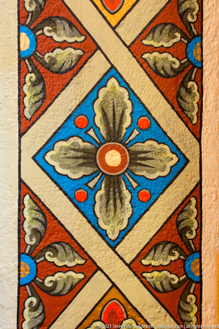 Painted geometric panel centers on a blue diamond with a stylized flower and repeated leaf motifs.