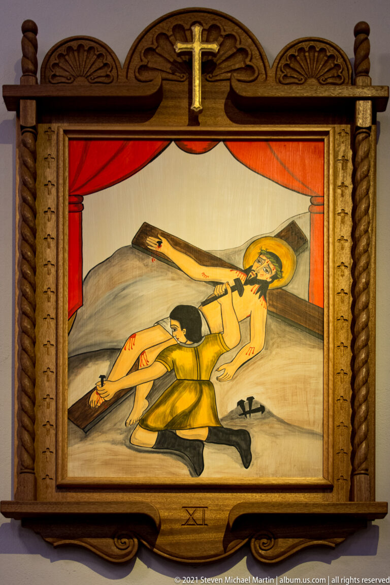 Framed painting shows Christ lying beside a cross as a man raises a hammer; XI appears below.