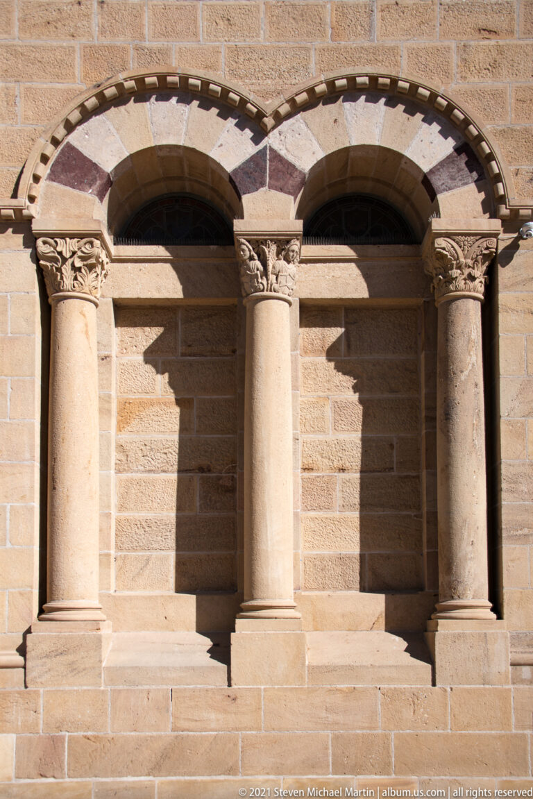 Two recessed stone arches with carved column capitals and alternating pale and reddish masonry.
