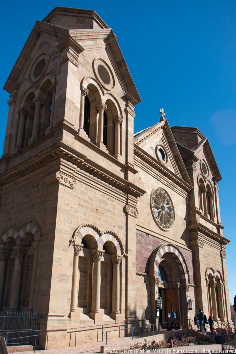 Twin-towered stone cathedral façade with a central rose window, arched entrance, and visitors below.