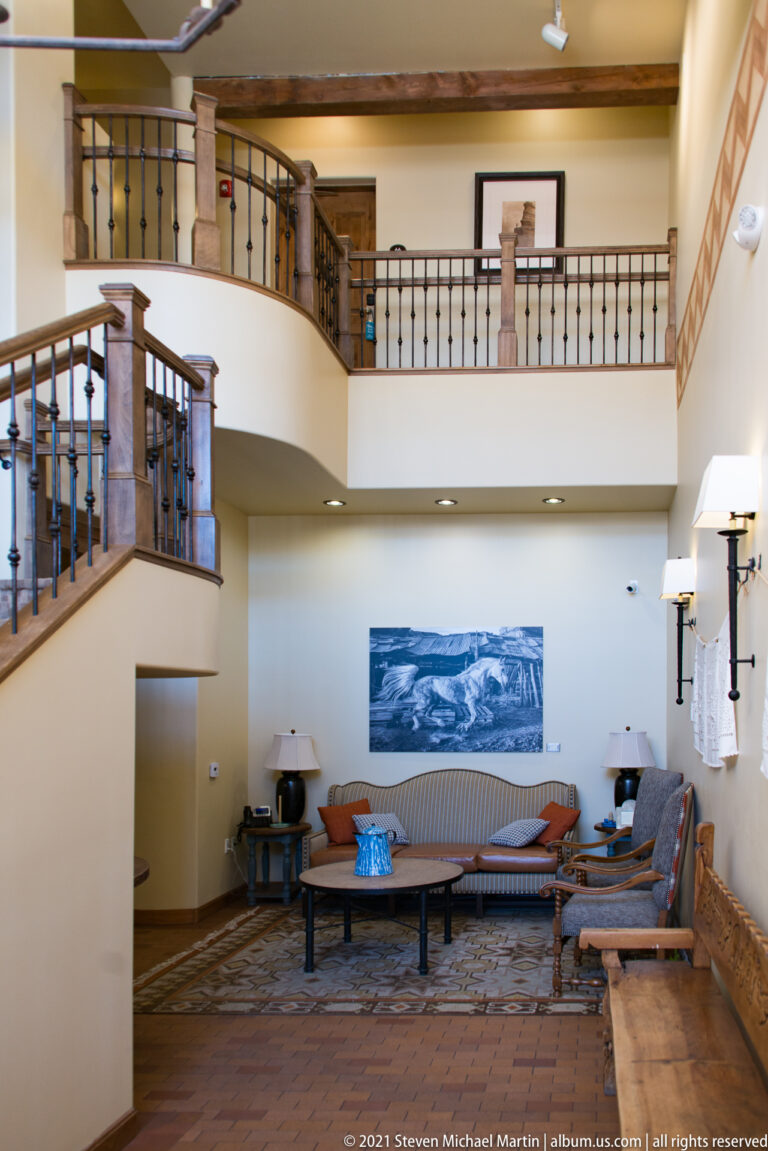 Sofas and chairs fill a lobby beneath a curved balcony with dark metal railings.