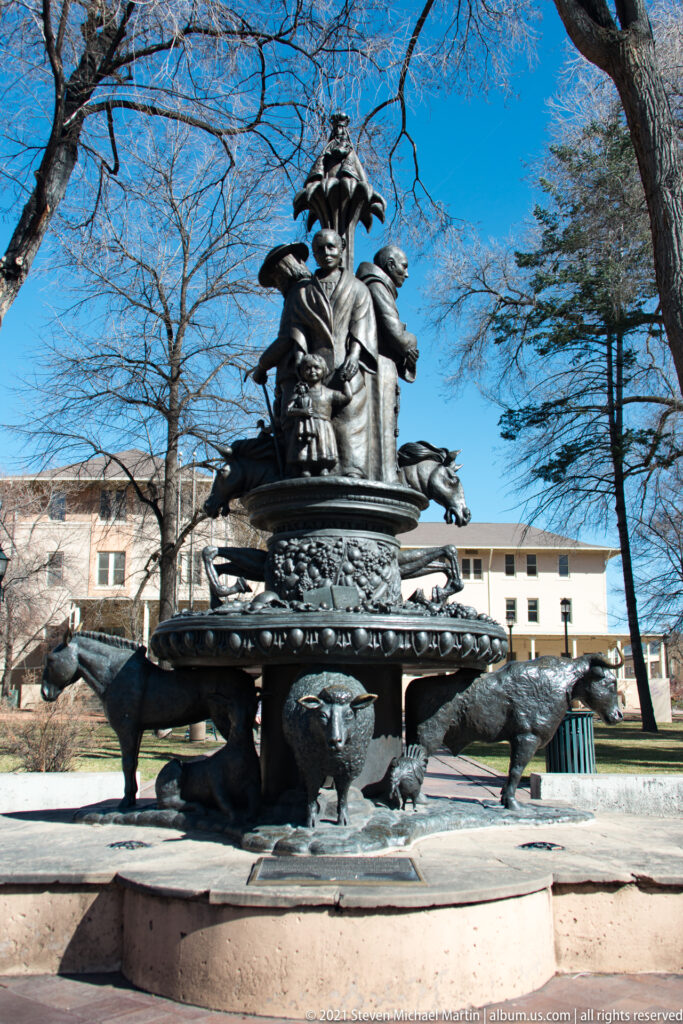Large bronze sculptural group with people and animal forms stands in a circular plaza basin.