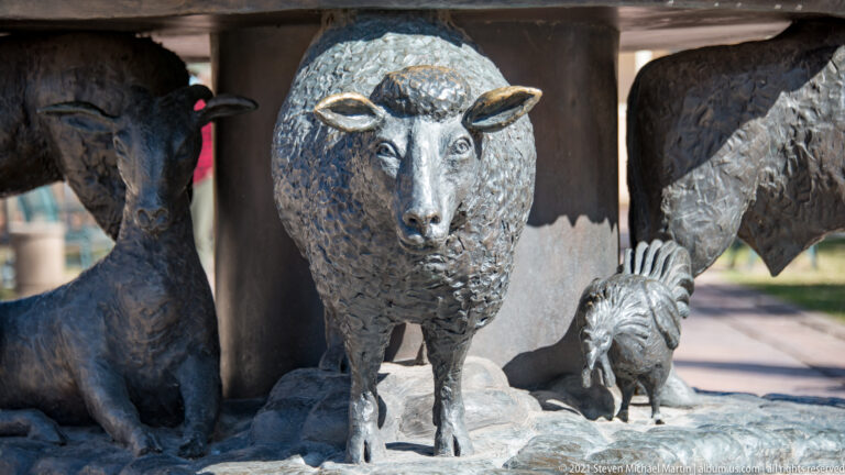 Close view of a woolly bronze animal standing among smaller animal figures on a sculptural basin.