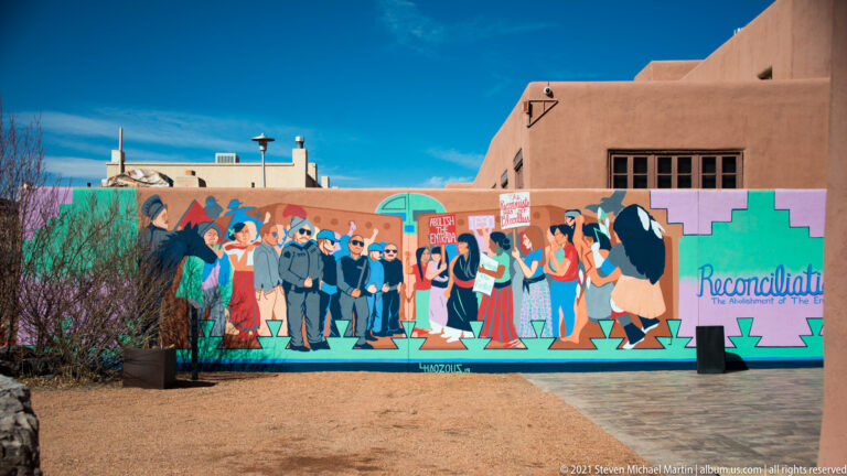 Long mural depicts a group of people beside the word “Reconciliation” on a colorful geometric background.