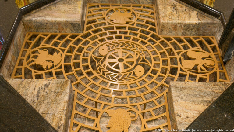 Overhead view of a circular floor inlay with radial lines, ring patterns, and four figurative medallions.