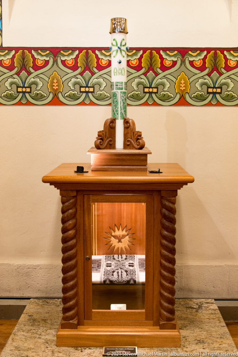 Wooden altar beneath a colorful floral frieze, with a central white column and framed devotional image.
