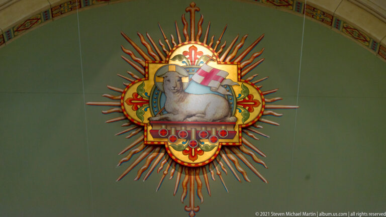 Painted ceiling emblem of a white lamb carrying a banner inside a red and gold sunburst.
