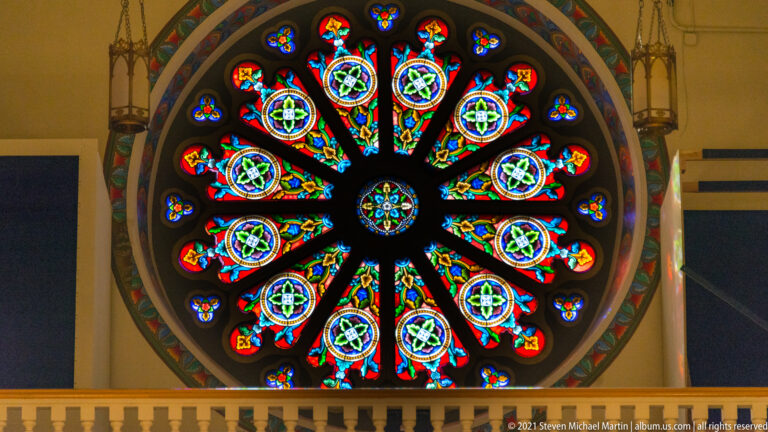 Close view of a circular stained-glass window with repeated blue, red, green, and gold radial panels.