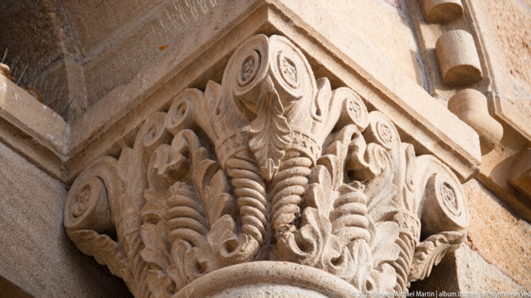 Low-angle close-up of a stone capital with leaf carving, curled volutes, and a patterned cornice.