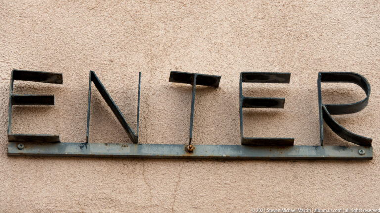 Dark raised letters spelling ENTER are mounted across a textured tan stucco wall.