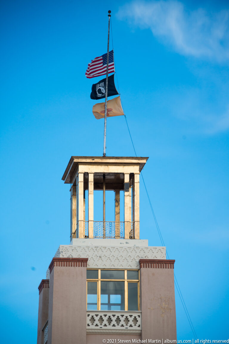 Civic building with a rooftop pavilion and United States and New Mexico flags against a blue sky.
