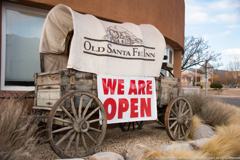 Covered wagon with wooden wheels and an Old Santa Fe Inn banner beside a “We Are Open” sign.