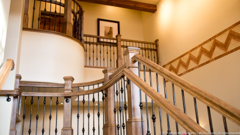 A wooden staircase with dark iron railings rises through an open two-story interior.