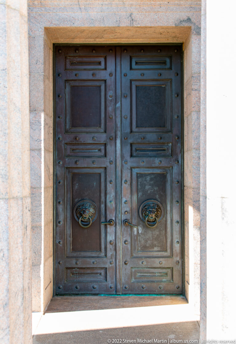 Two bronze-colored doors with rectangular panels and circular handles sit in a pale stone frame.