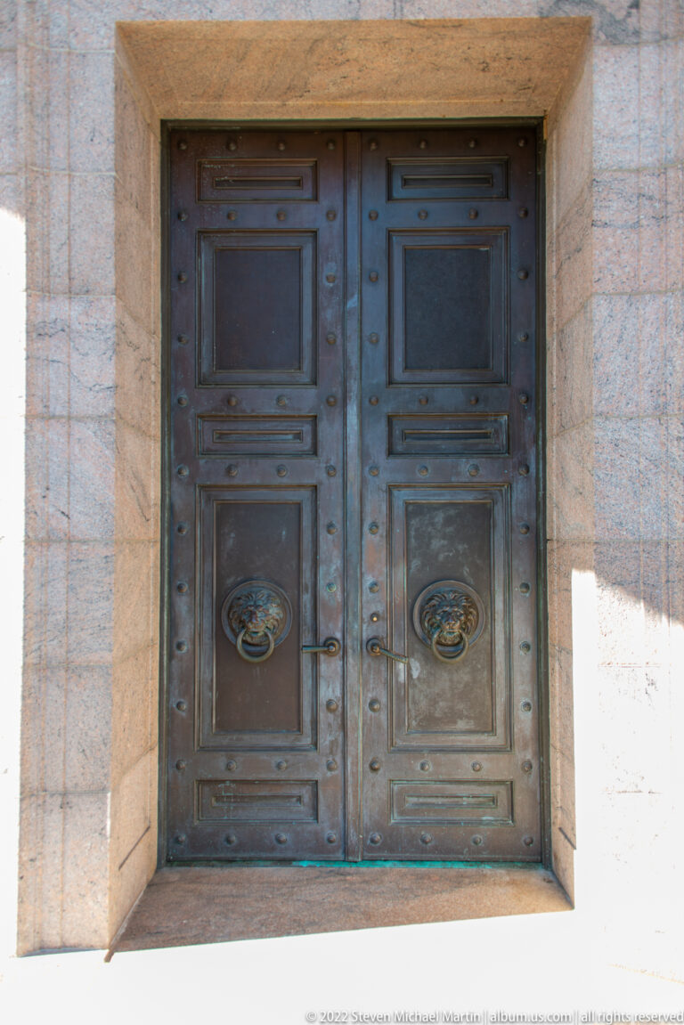 Paired dark doors with circular sculpted handles fill a pale stone entrance recess.