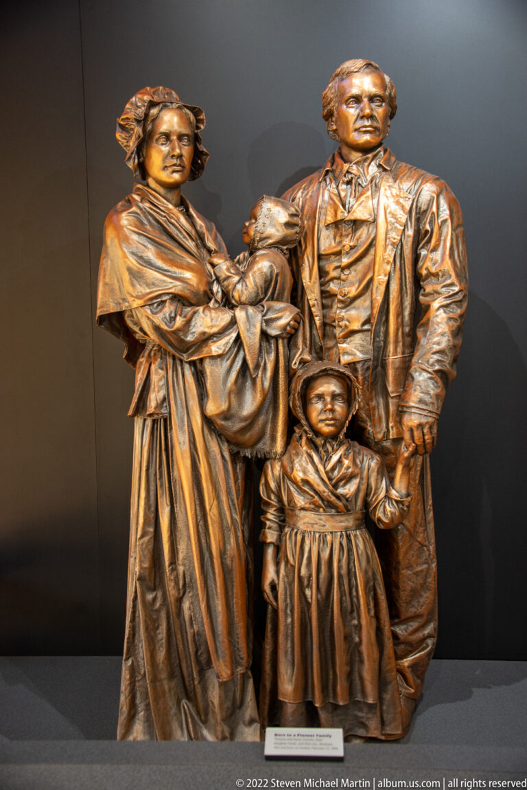 A bronze sculpture shows a woman and man standing behind a child in period-style clothing.