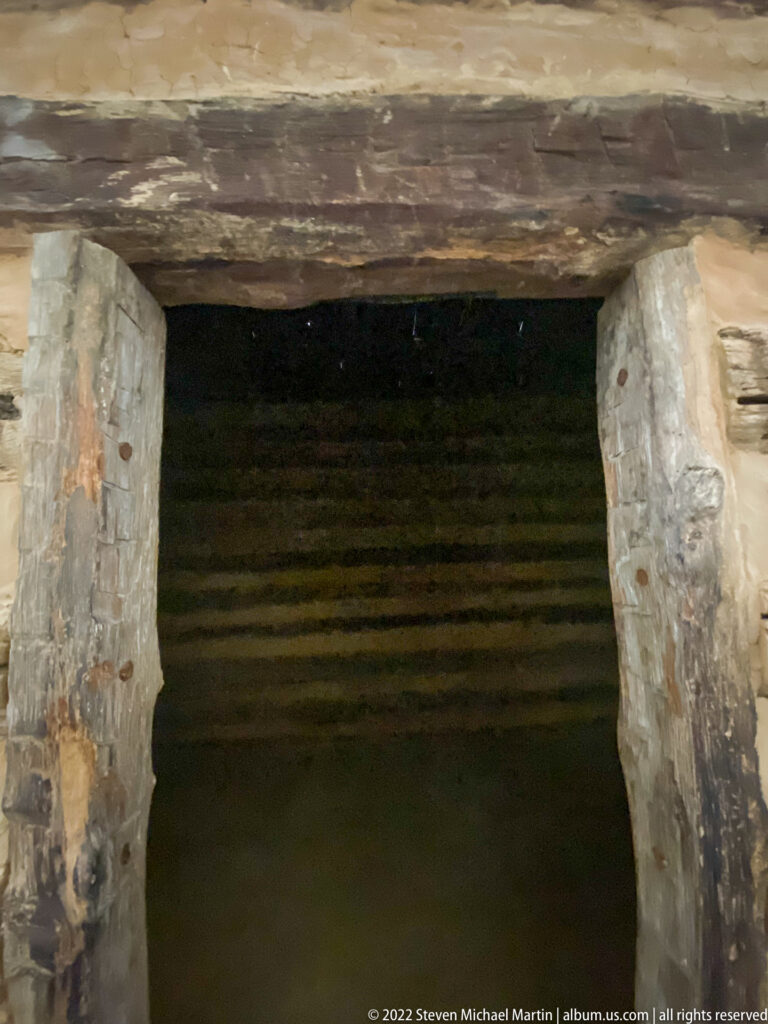 A low rectangular doorway framed by heavy logs and stone opens into a dark cabin interior.
