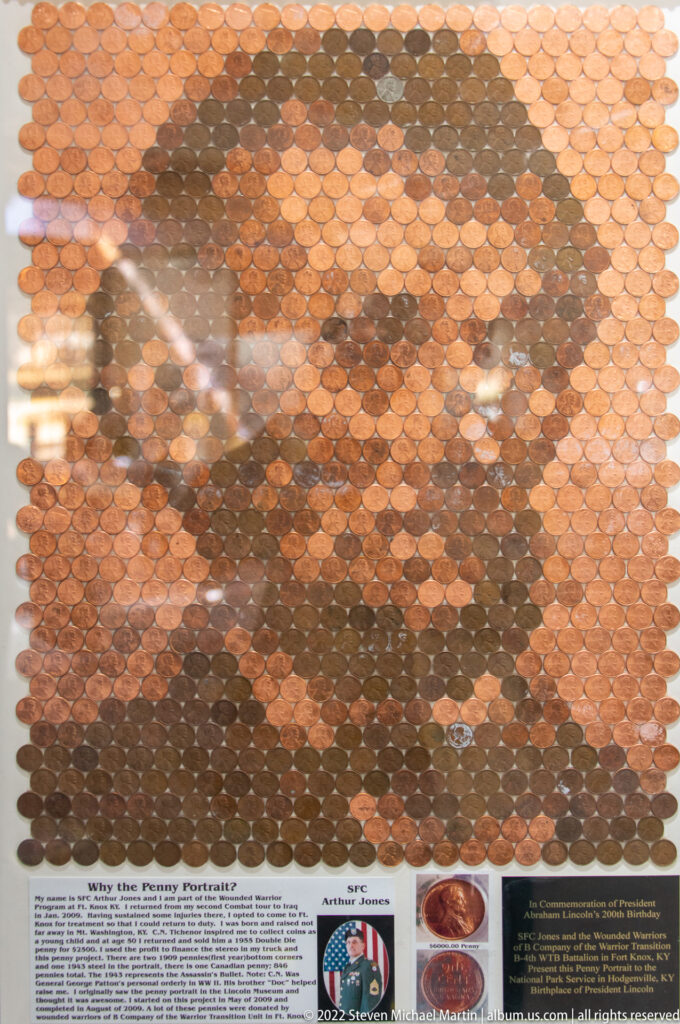 Rows of copper pennies cover a panel around a circular portrait medallion and a small interpretive label.