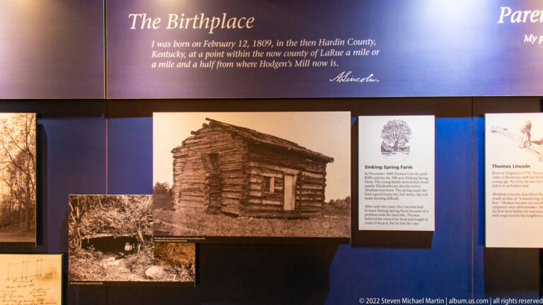A sepia log cabin photograph fills a “The Birthplace” exhibit wall beside family-history panels.