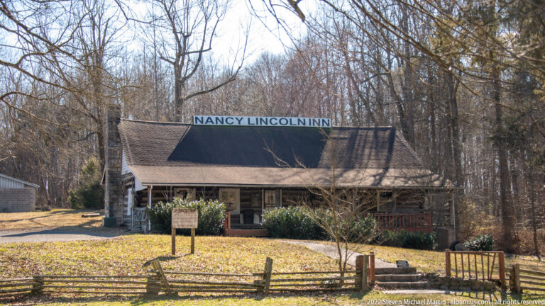 A low building labeled Nancy Lincoln Inn stands behind a split-rail fence among bare trees.