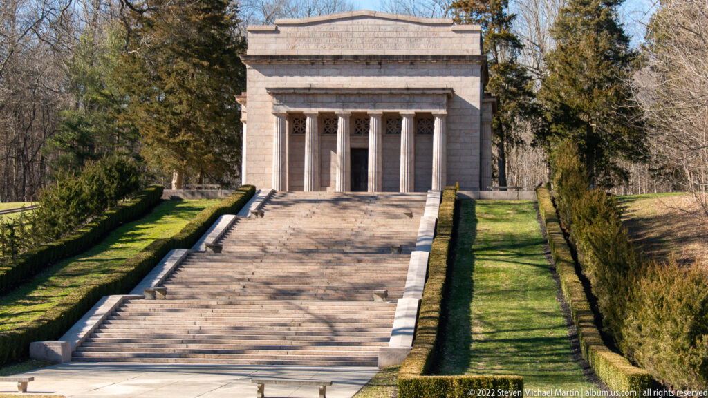 The memorial’s central portico aligns with a long staircase bordered by clipped hedges and trees.