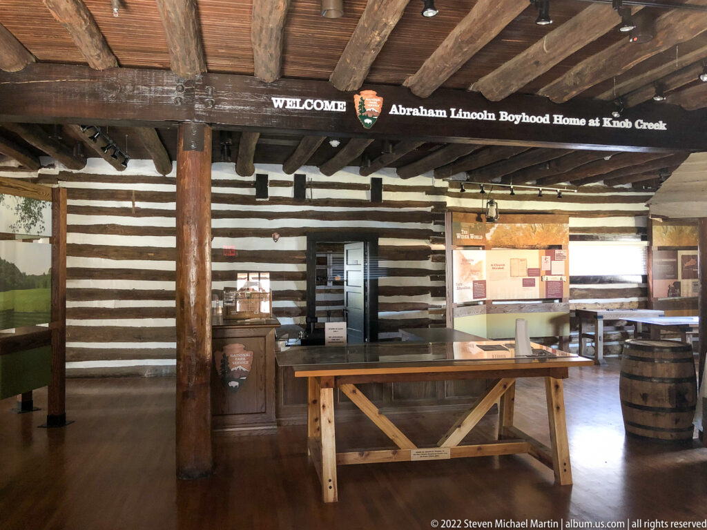 Exposed beams, log walls, exhibit tables, and a welcome sign fill the visitor room at Knob Creek.