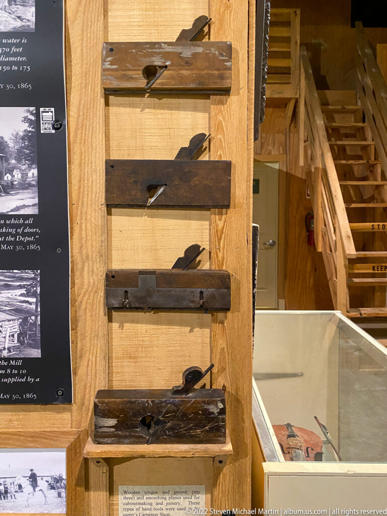 Wooden hand planes with metal blades hang vertically on a timber wall beside a gallery staircase.